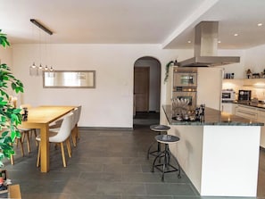 A modern kitchen with a dining area, featuring a central island with stools, a large mirror, pendant lights, and built-in appliances. - Amore Appartement/Fewo, Dusche und Bad, WC, 6-Bettwohnung by Interhome (Arosa)