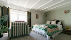 Un dormitorio con cama, una silla, una ventana con cortinas, una planta y una lámpara de pared.