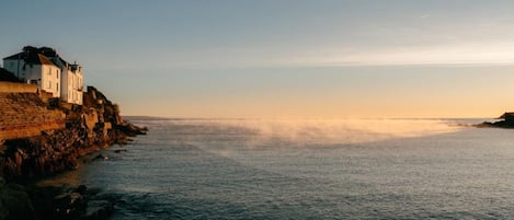 Un edificio frente al mar, situado en un acantilado, con vista a un mar tranquilo.