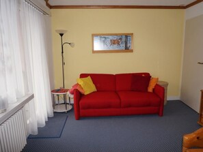 Une pièce avec un canapé rouge, une petite table ronde, un lampadaire et un tableau accroché au mur.