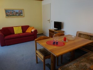 Un salon avec un canapé rouge, une table à manger en bois et un téléviseur.