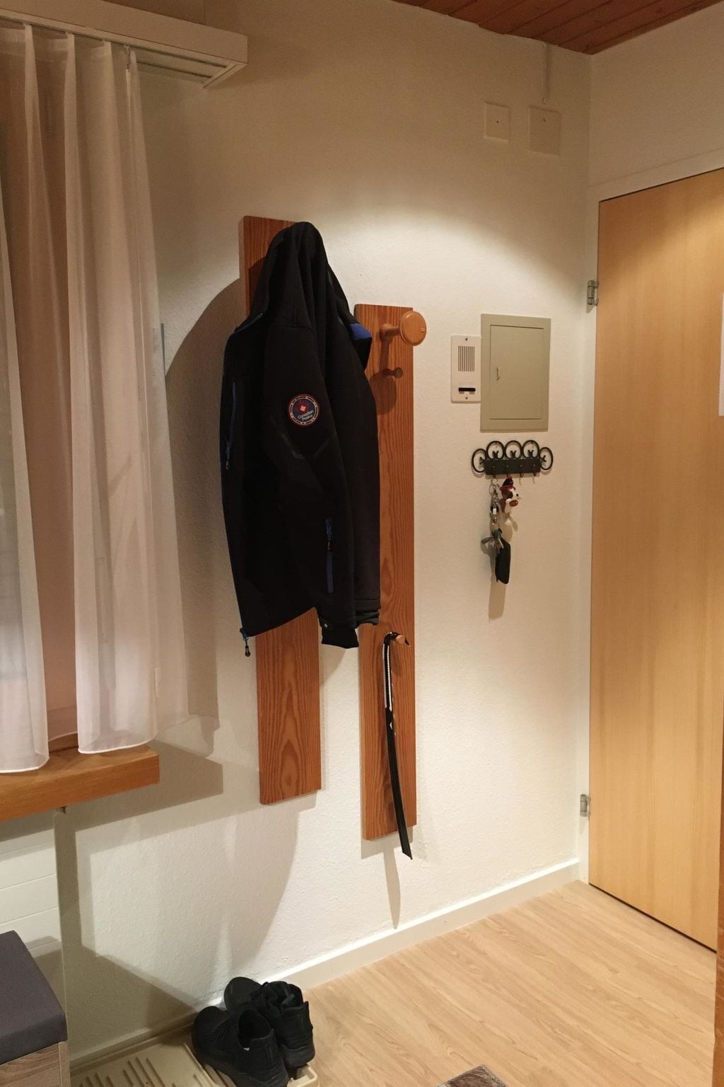 A room with a coat rack, a door with a key lock, and a wall-mounted key holder.