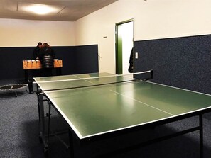 A ping pong table in a room with a dark floor, a door, and a person standing near a table tennis table. - I dr Rehwiesa C31 Appartement/Fewo, Bad, WC, 4-Bettwohnung by Interhome (Arosa)