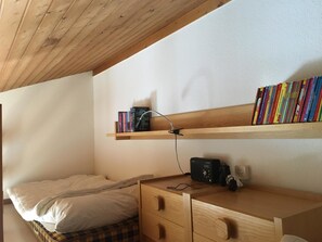 A bedroom with a bed, a wooden desk, a shelf with books, and a radio. - I dr Rehwiesa C31 Appartement/Fewo, Bad, WC, 4-Bettwohnung by Interhome (Arosa)