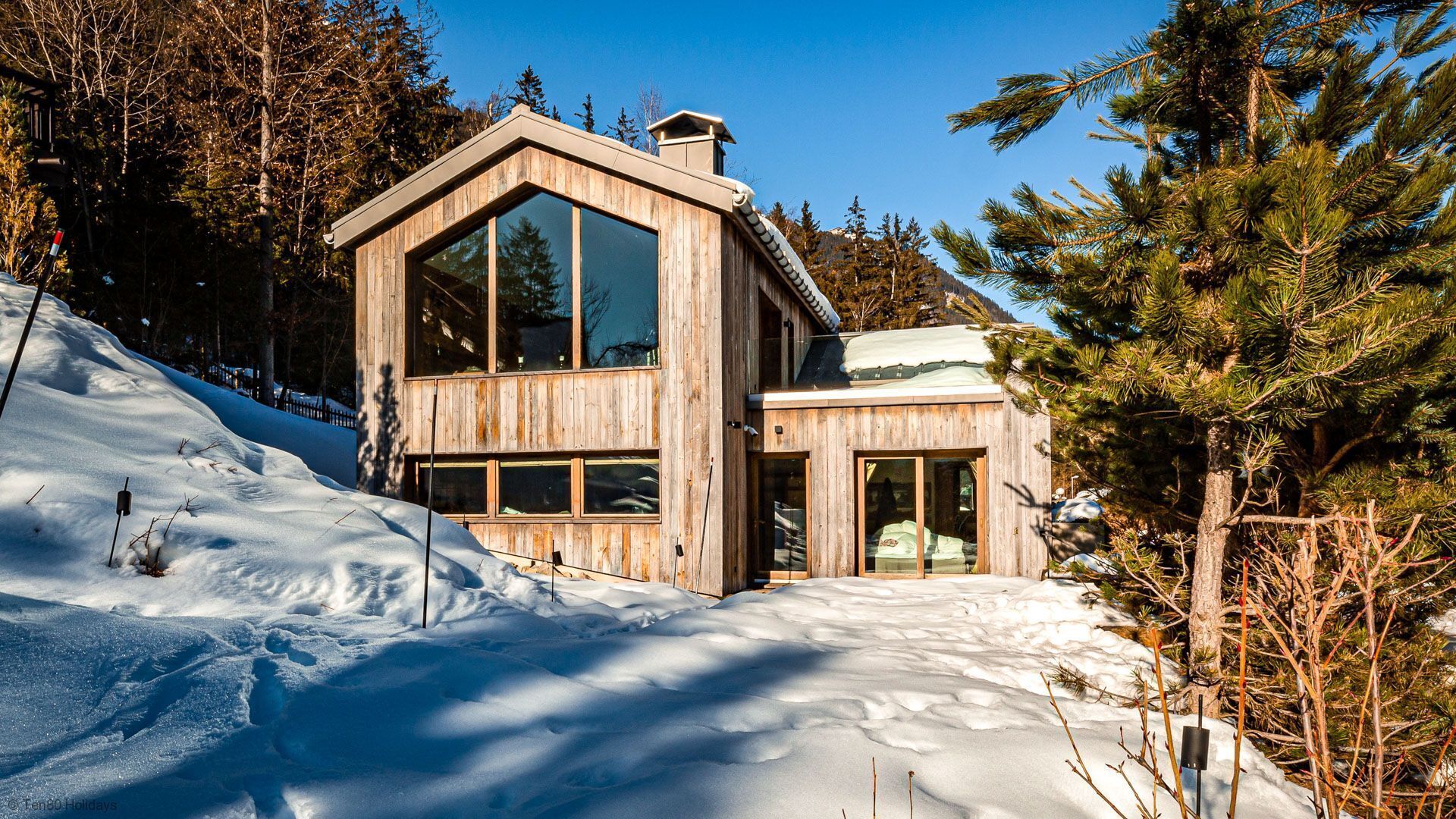 Eine Holzhütte mit großen Fenstern, umgeben von Schnee und Bäumen.