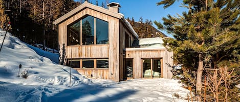 Eine Holzhütte mit großen Fenstern, umgeben von Schnee und Bäumen.