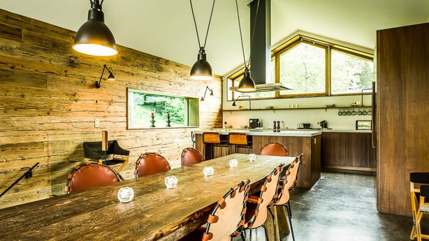 A modern kitchen with a wooden wall, a dining area with a large wooden table and leather chairs, and pendant lighting. - Chalet Noyer - Luxury 4 bedroom chalet only a short walk from Chamonix centre (Chamonix)