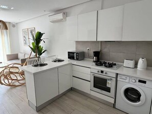 A modern kitchen with white cabinetry, a built-in oven, a microwave, a coffee maker, and a washing machine. - B15 Cozy Apartment in La Marsa (La Marsa)