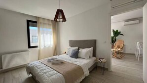 Un dormitorio moderno con una cama grande, una mesita de noche, una lámpara colgante y vistas al exterior a través de una ventana.