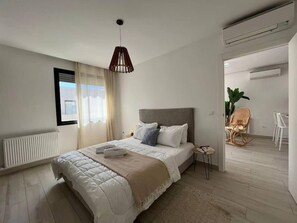 A modern bedroom with a large bed, a bedside table, a hanging light fixture, and a view of the outside through a window. - B15 Cozy Apartment in La Marsa (La Marsa)