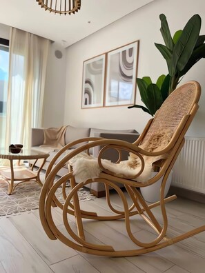 A modern living room with a wicker rocking chair, a sofa, and a coffee table. There are abstract paintings on the wall and a large plant. - B15 Cozy Apartment in La Marsa (La Marsa)