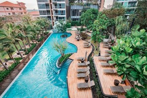 A swimming pool with a wooden deck, lounge chairs, and tropical plants. - 2 Bedroom High Floor Sea View Unit (Pattaya)