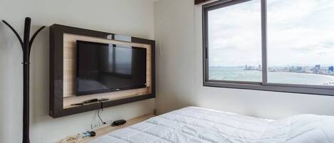 Una habitación de hotel con cama, televisor montado en la pared, ventana con vistas a la ciudad y escritorio con silla.
