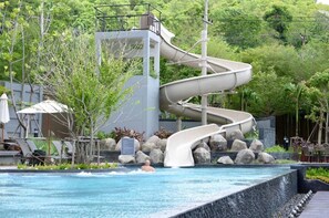 A pool with a multi-level water slide, surrounded by rocks and greenery. - 2 Bedroom High Floor Sea View Unit (Pattaya)