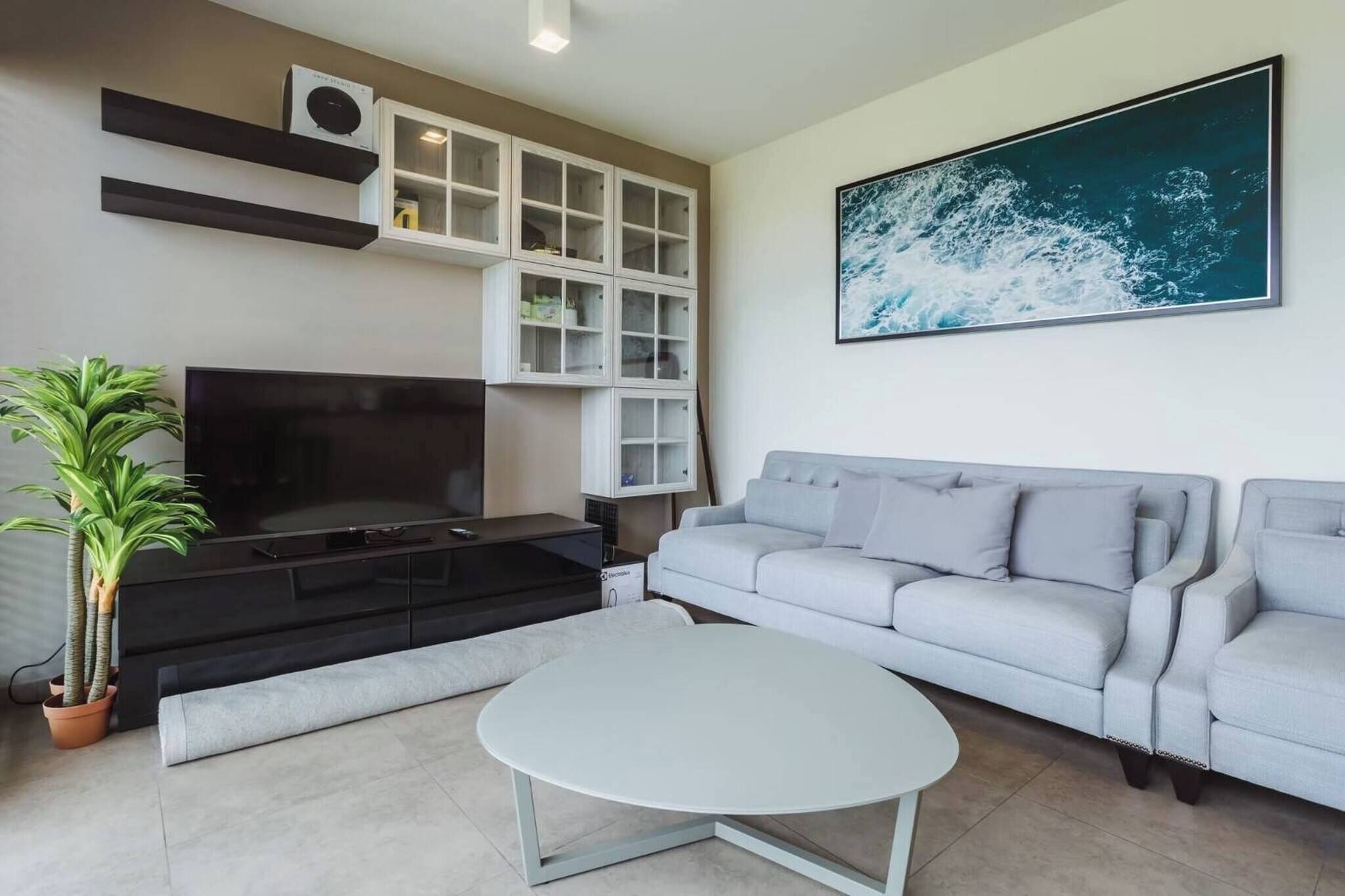 Una sala de estar con un televisor de pantalla plana, un sofá gris, una mesa de centro blanca y un cuadro abstracto grande en la pared.