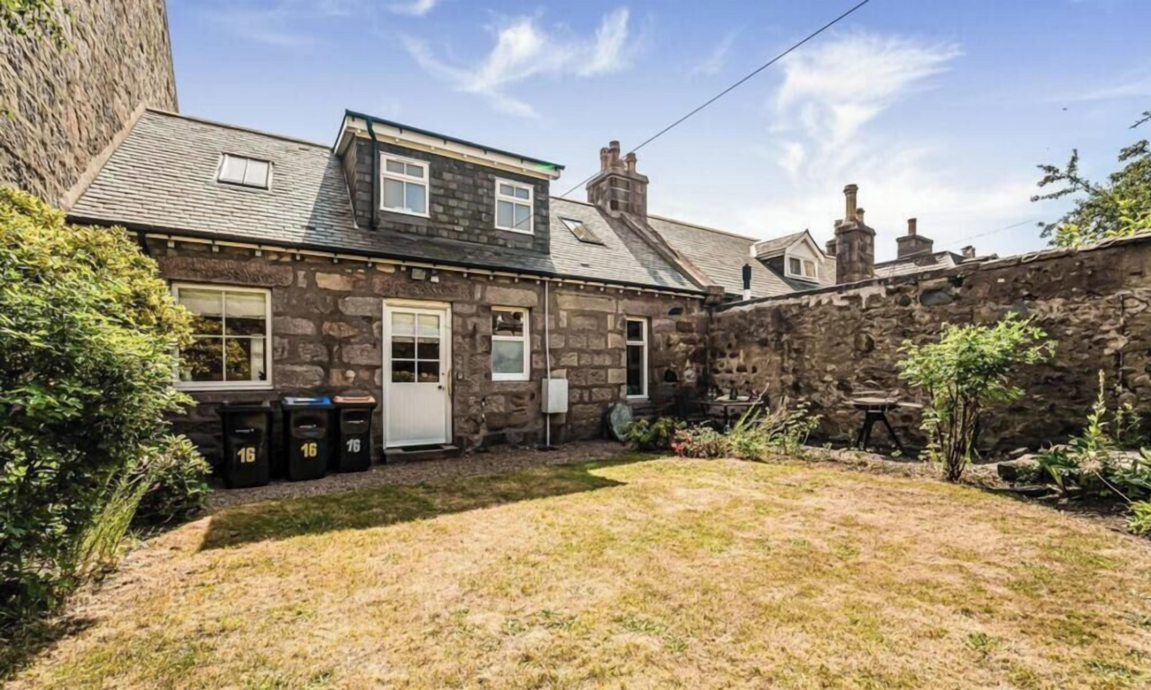 A stone house with a sloped roof, a front door, and a small front yard.