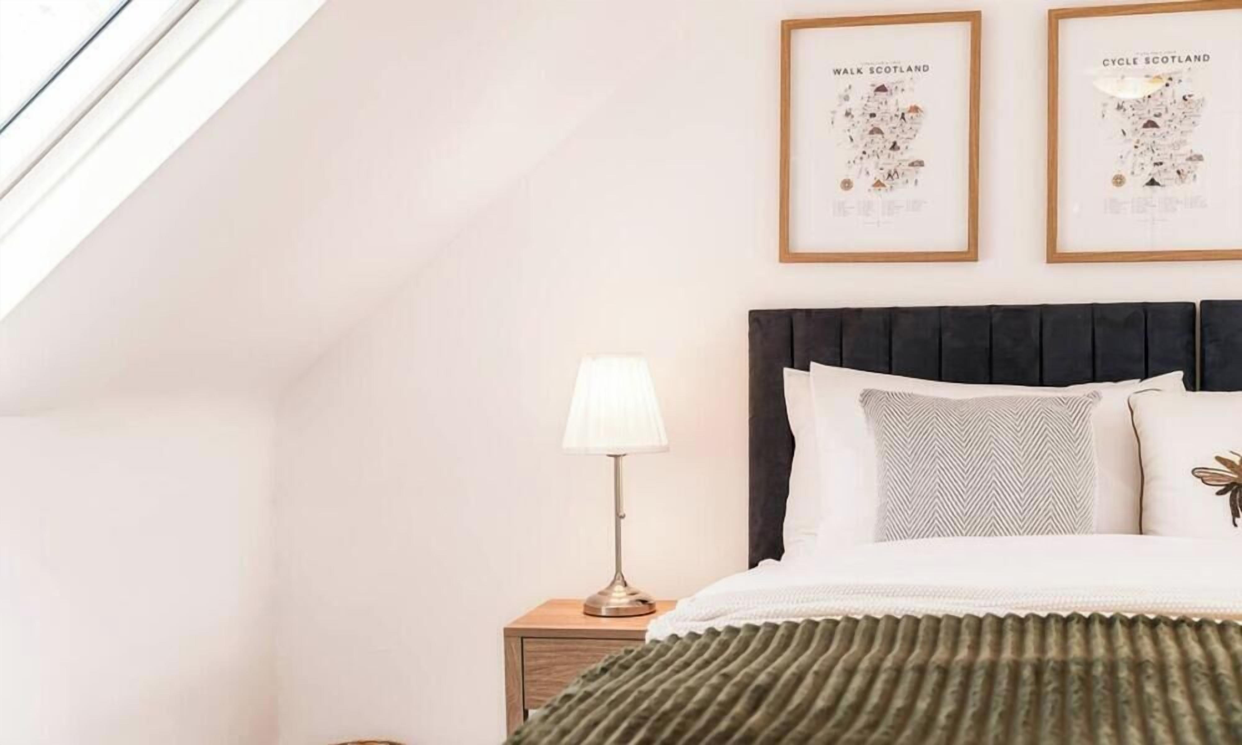 A bedroom with a bed, a nightstand, a lamp, and two framed maps on the wall.