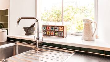 A kitchen with a stainless steel sink, a stone mortar, a colorful tile tray, and a white pitcher on the window sill.