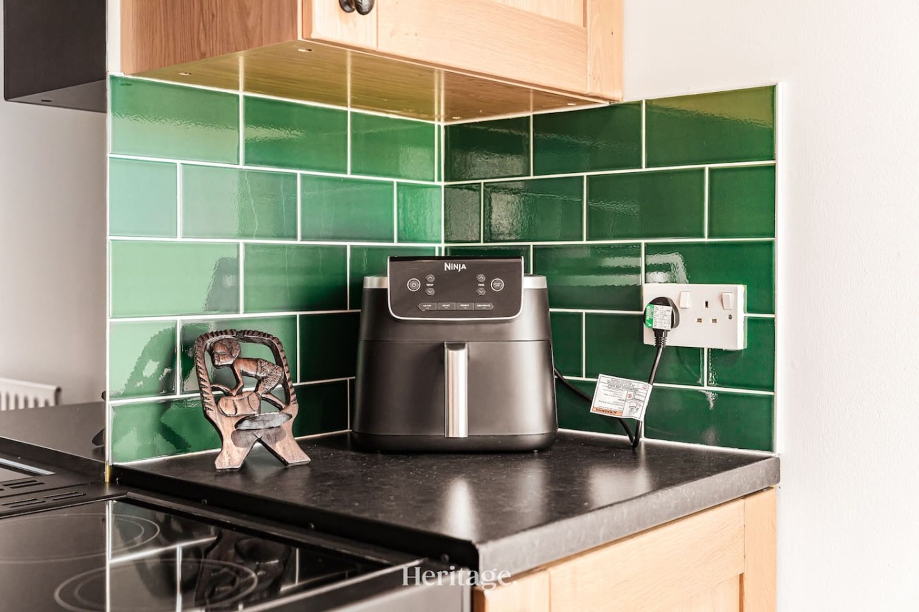 A kitchen with a black Ninja coffee maker on the counter, green tiled backsplash, and a small wooden sculpture.