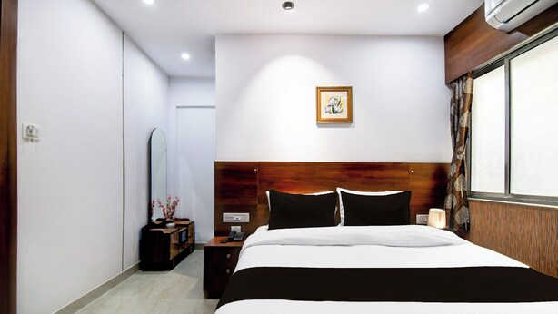 Une chambre d’hôtel avec un grand lit, une tête de lit en bois, une table de chevet avec une lampe, un miroir et un tableau encadré au mur.