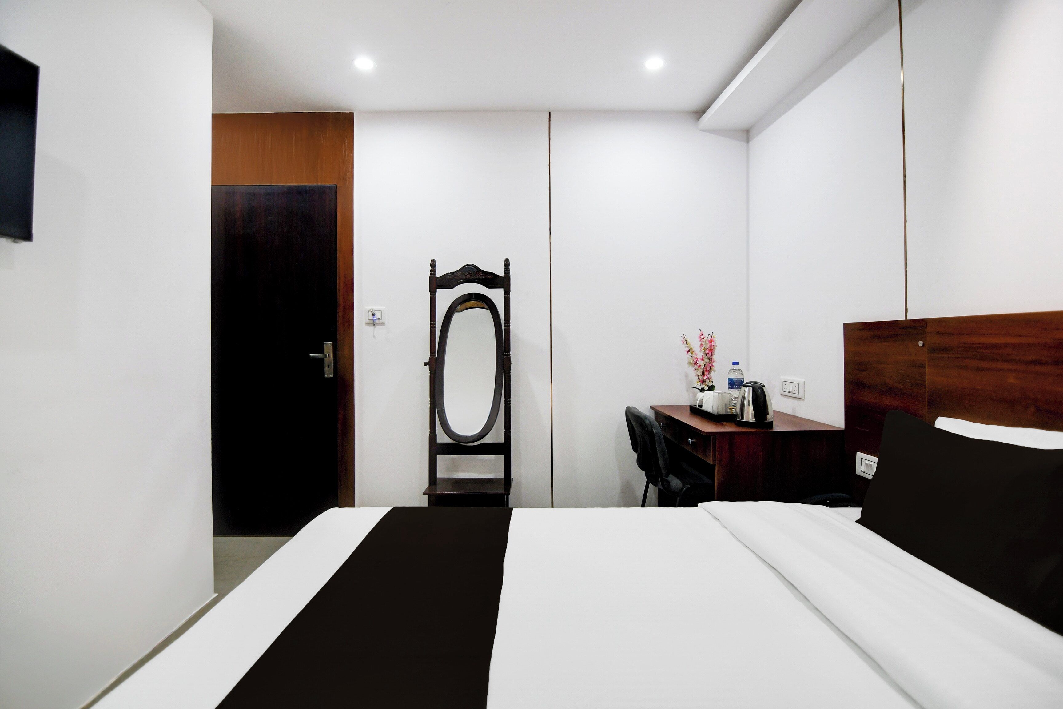 Habitación de hotel con cama, escritorio, silla, espejo y puerta.