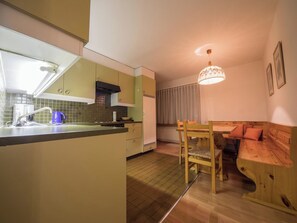 A compact kitchen with a built-in island, a dining area with a bench, and a pendant light. - I dr Rehwiesa A16 Appartement/Fewo, Bad, WC, 4-Bettwohnung 4-Bettwohnung by Interhome (Arosa)