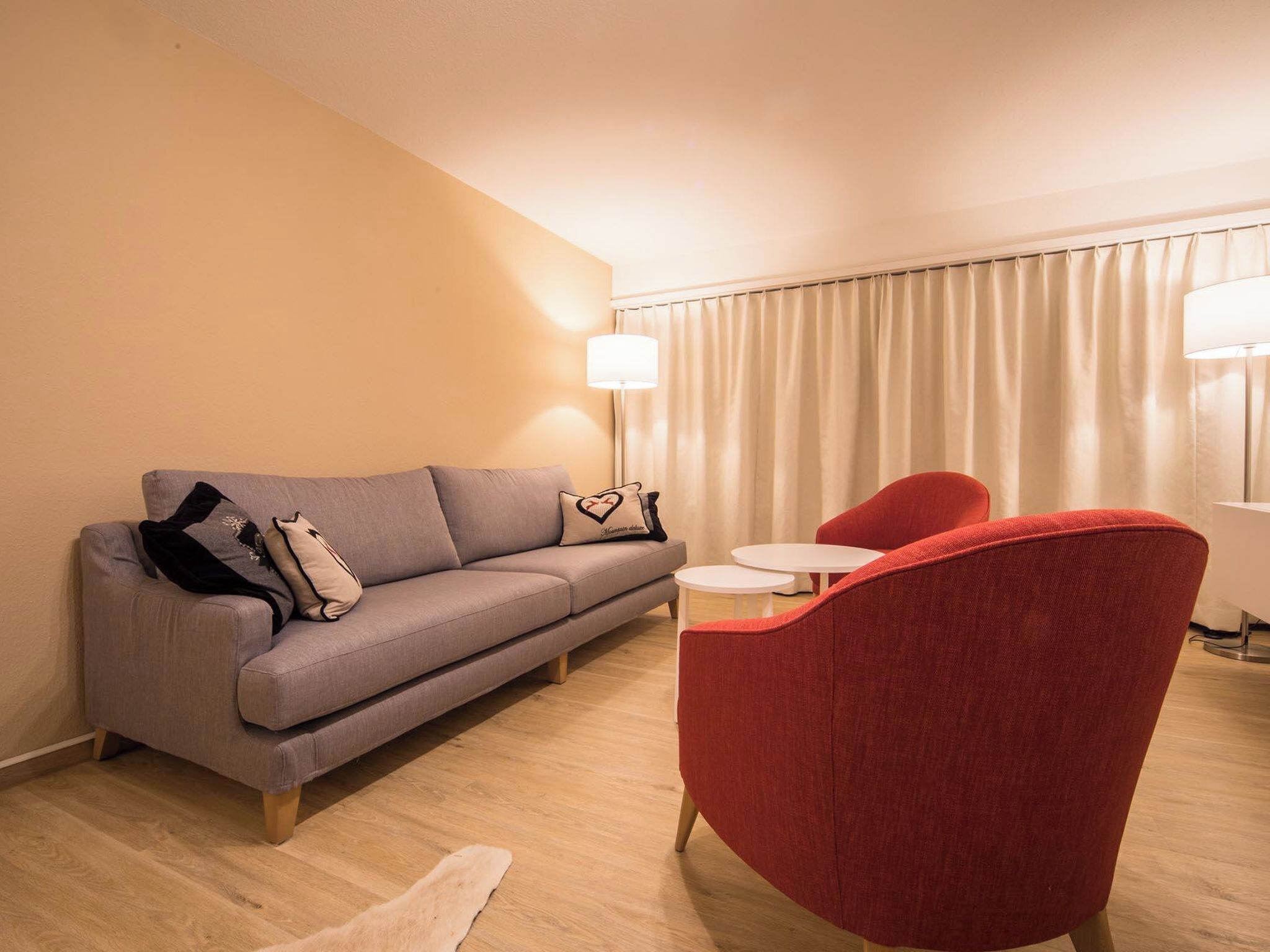 Ein modernes Wohnzimmer mit einem grauen Sofa, einem roten Sessel, einem kleinen runden Tisch und einer Stehlampe.