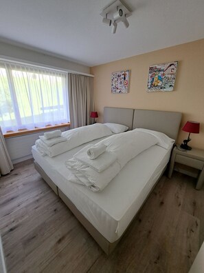 A hotel room with a large bed, two bedside lamps, a window with curtains, and two wall art pieces. - I dr Rehwiesa A16 Appartement/Fewo, Bad, WC, 4-Bettwohnung 4-Bettwohnung by Interhome (Arosa)