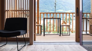 Terraza de madera con una silla negra y una mesa pequeña, con vistas a un paisaje montañoso.
