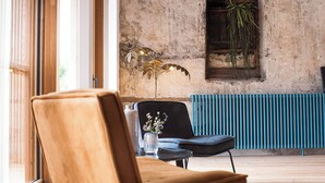 Una habitación con un ventanal grande, un radiador, una planta y una silla.
