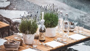 Mesa de comedor al aire libre con copas de vino, una botella y macetas con plantas.