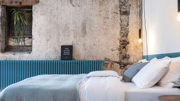 Une chambre avec un mur en pierre, une plante suspendue, un panneau décoratif, un lit avec une literie blanche et une tête de lit bleue.