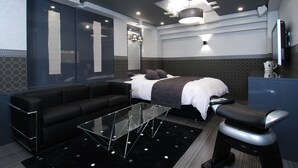 Ett modernt hotellrum med en säng, en soffa, ett soffbord i glas och en TV.