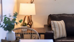 En stue med en mørk lædersofa, et hvidt bord, en lampe og en plante.