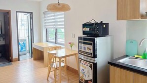 A compact kitchen with a refrigerator, microwave, and a sink. There's a dining table with chairs and a hanging light fixture. - Reveur Apartment (Da Nang)