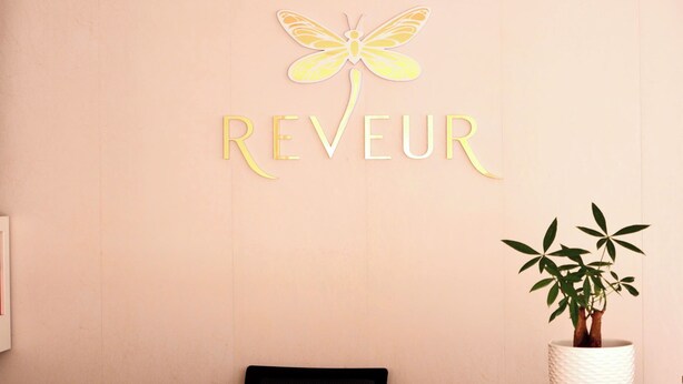 A reception desk with a wall-mounted sign reading "REVEUR" and a decorative yellow dragonfly. - Reveur Apartment (Da Nang)