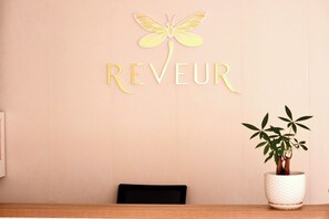 A reception desk with a wall-mounted sign reading "REVEUR" and a decorative yellow dragonfly. - Reveur Apartment (An Hai)