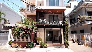 An apartment building with a sign reading "REVEUR APARTMENT" and a butterfly logo. There are potted plants and flowers in front, and a motorcycle parked outside. - Reveur Apartment (Da Nang)