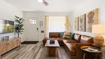Un salon avec un canapé en cuir marron, une table basse en bois, un téléviseur et une plante.