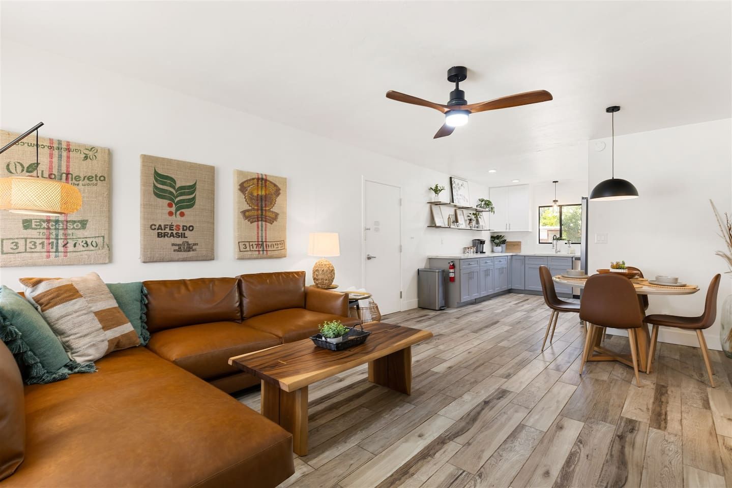 A modern living room with a brown leather sofa, wooden coffee table, and a dining area with a table and chairs.