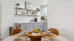 Un comedor con una mesa dispuesta para cuatro, una cocina al fondo y un extintor en el suelo.