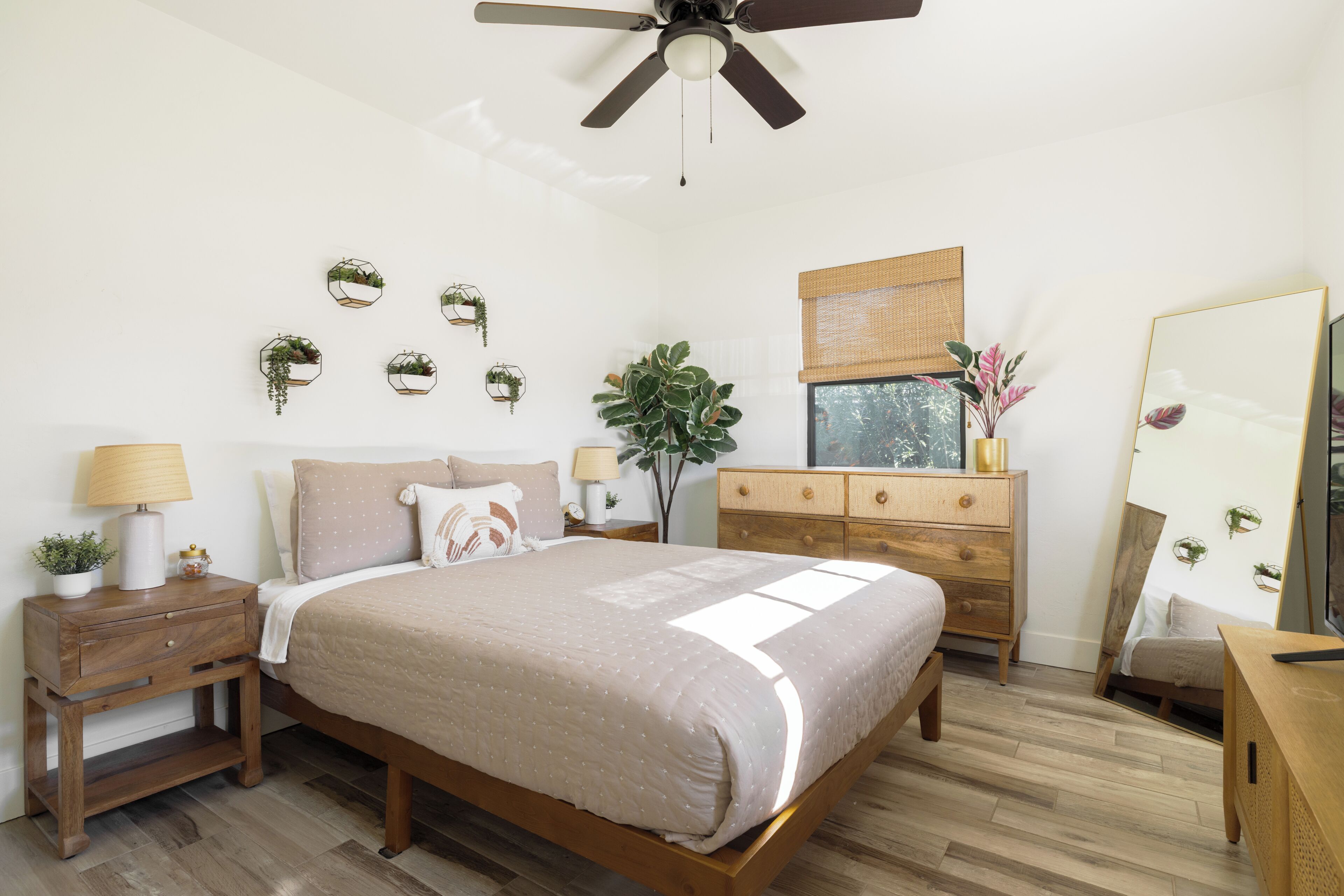 A bedroom with a bed, bedside tables, a dresser, a ceiling fan, and wall-mounted planters.