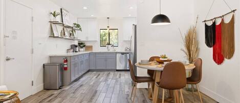 A modern kitchen with grey cabinets, a stainless steel refrigerator, and a dining area with a round table and brown chairs.