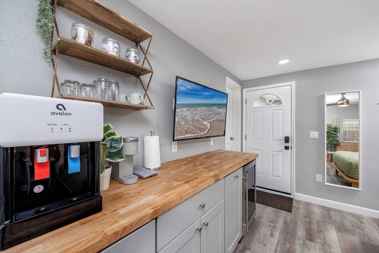 A modern kitchen with a coffee machine, a wooden countertop, and a shelf with jars.