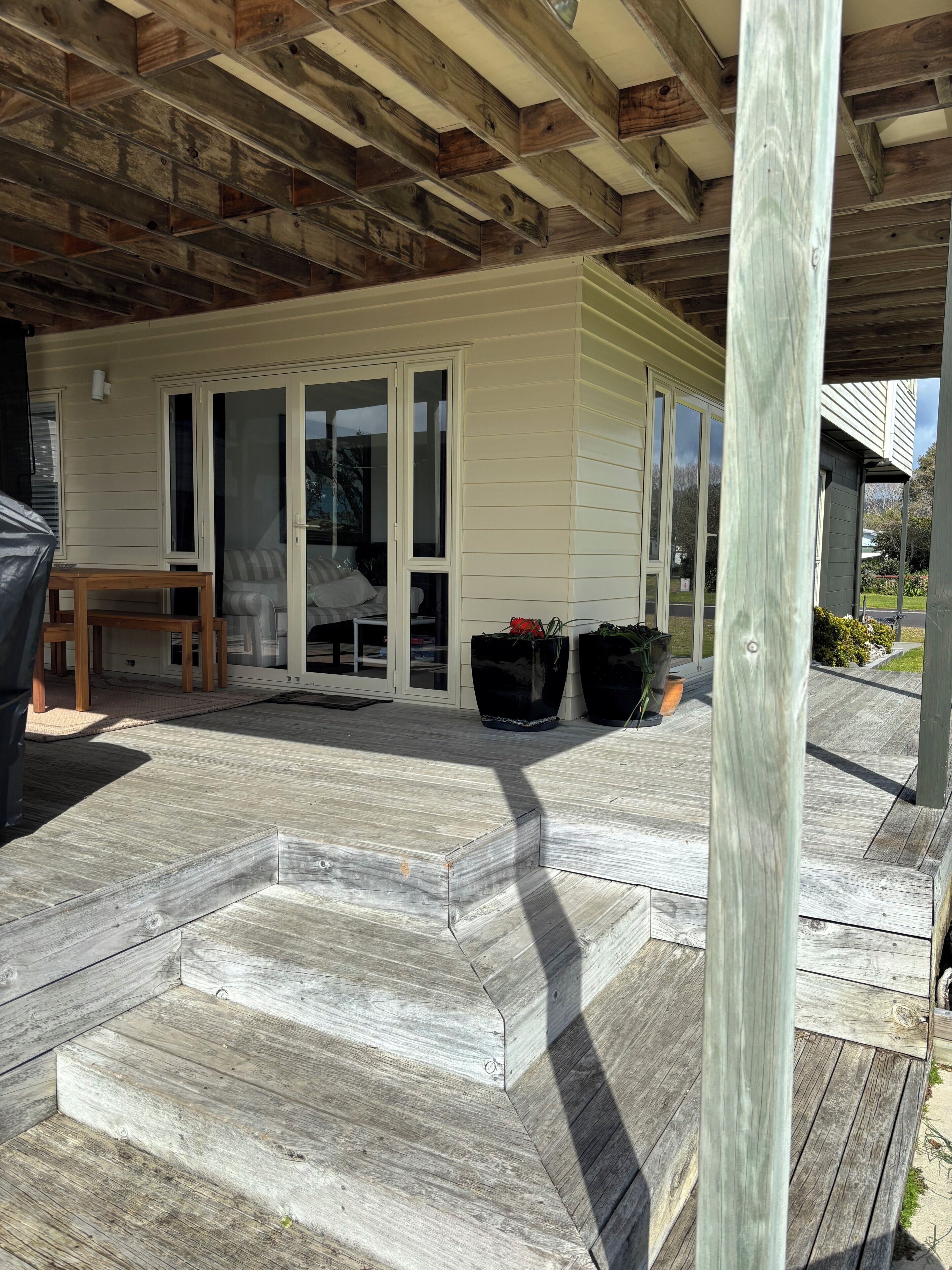 Uma área externa coberta com deck de madeira, uma porta de correr e plantas em vasos.