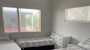 Een slaapkamer met drie bedden, een kapstok en een raam met jaloezieën.