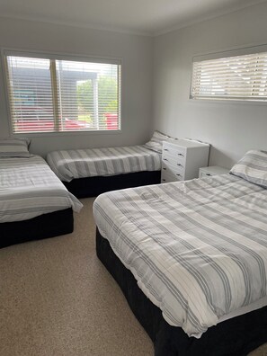 A bedroom with three beds, a dresser, and a window with blinds. - Whitianga downstairs flat with car & boat parking close to beach (Whitianga)
