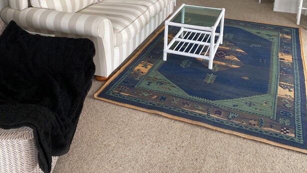 Een woonkamer met een gestreept bankje, een glazen salontafel, een kamerkleed met een patroon en een schilderij van bomen.
