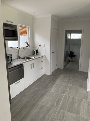 A modern kitchen with white cabinets, stainless steel appliances, and a grey tiled floor. - Whitianga downstairs flat with car & boat parking close to beach (Whitianga)