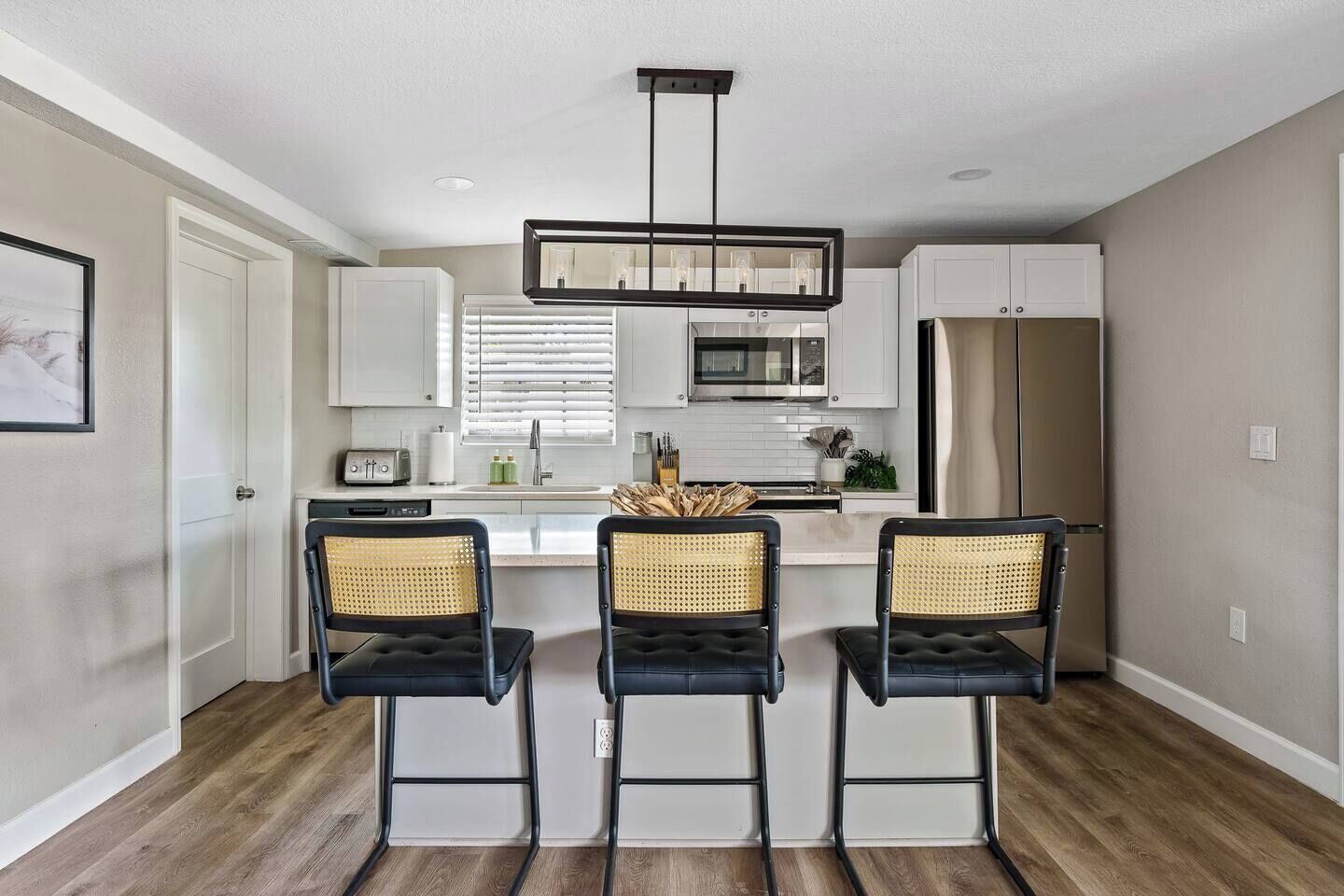 A modern kitchen with white cabinets, a central island with bar stools, and a hanging light fixture.